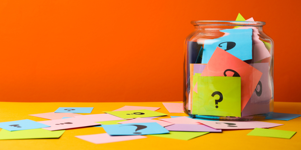 Colorful cards with question marks in glass jar on orange background. Space for text